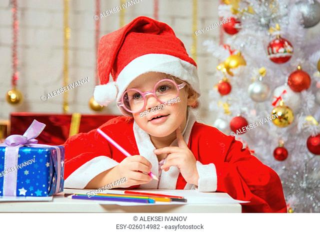 Four-year girl dressed in a red suit Santa Claus draws pencils are in a festive Christmas interior
