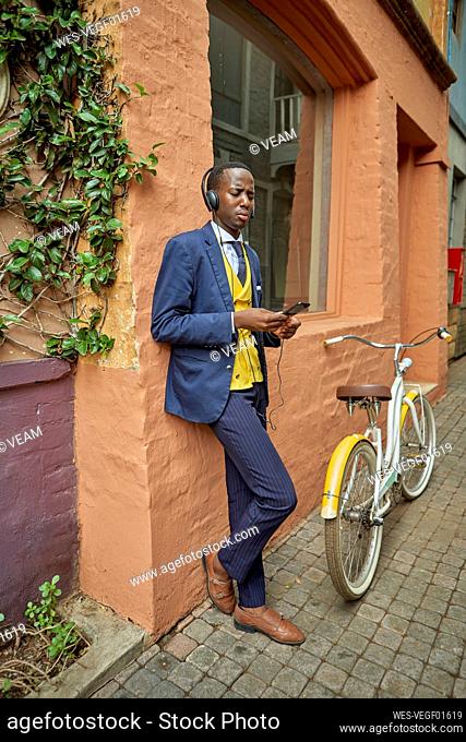 Stylish young businessman with bicycle wearing old-fashioned suit listening to music on his headphones
