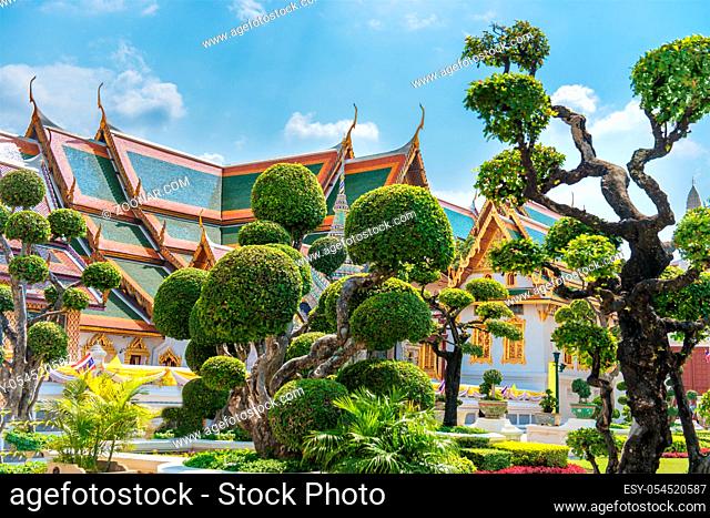 Topiary garden with trimmed trees on green lawn in front of Grand Palace in Bangkok, Thailand