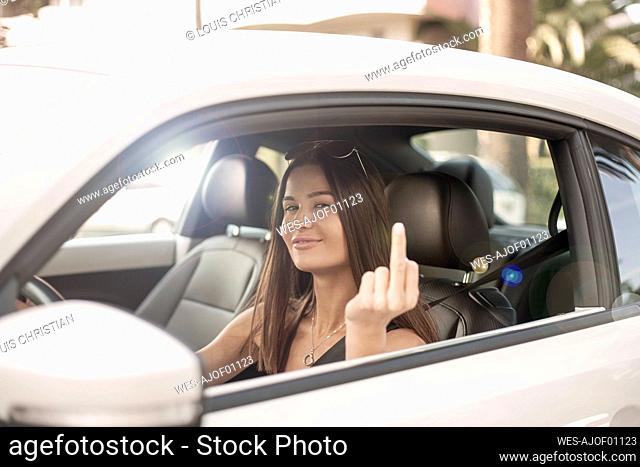 Smiling beautiful woman showing middle finger while driving car