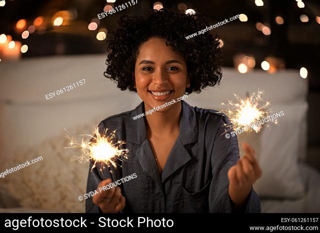 happy woman with sparklers sitting in bed at night