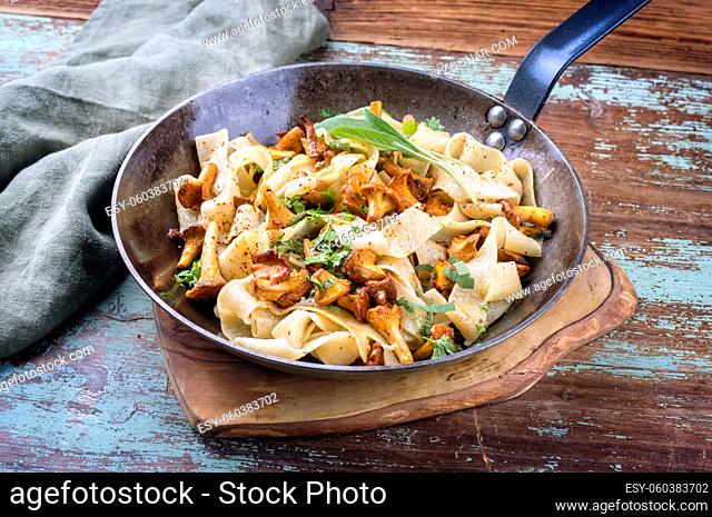 Traditional fried Italian tagliatelle con galletti with mushrooms offered as close-up in a rustic iron pan