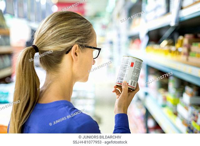 Woman studying label on wet canned food can in front of a shelf in a store. Germany