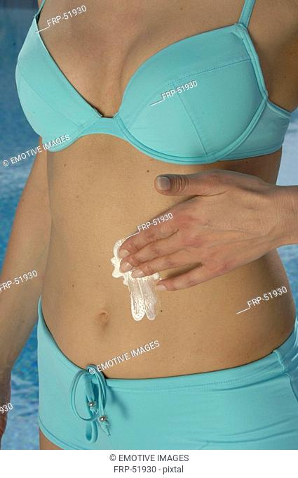 Woman in a turquoise bikini is applying sunlotion on her belly