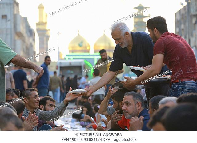 23 May 2019, Iraq, Baghdad: Men distribute food for people who gathered for a free public Iftar meal during the Muslim holy month of Ramadan at the Kadhimiya...