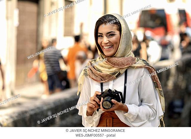 Spain, Granada, young Arab tourist woman wearing hijab, using camera during sightseeing in the city