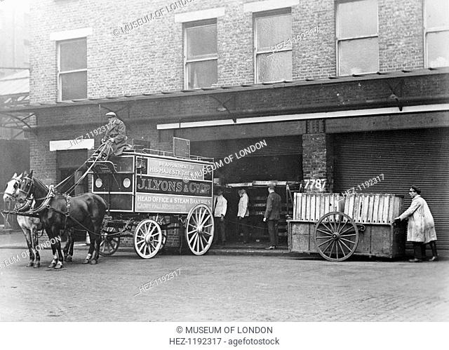 A horse drawn Lyons van, Cadby Hall, West Kensington, London. Standing outside the depot while trays of bread are loaded into the back