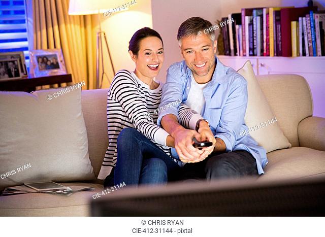 Playful couple fighting over remote control watching TV in living room