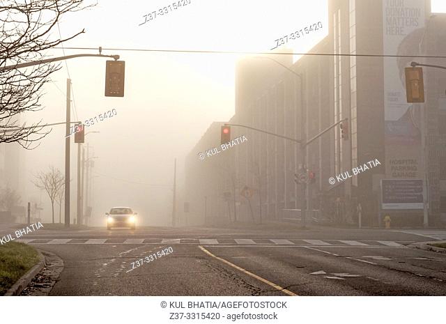 One car stopped at a red traffic light at an intersection in heavy fog, Canada