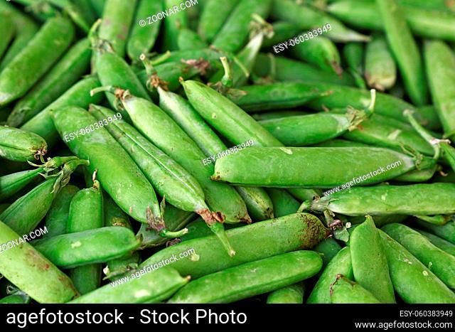Close up fresh spring green peas pods on retail display of farmers market, high angle view