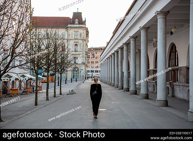 Rear view of unrecognizable woman walking in empty old medieval Ljubljana city center during corona virus pandemic. Almost no people outside on streets