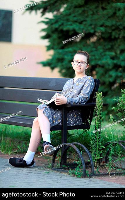 Pensive girl sits on a bench with book in her hands. Selective focus
