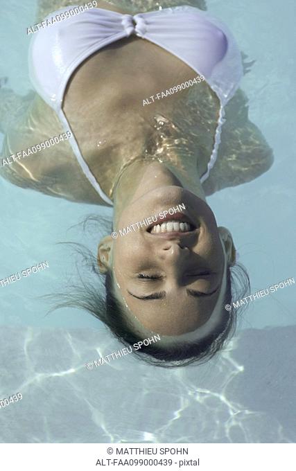 Young woman floating in swimming pool, smiling