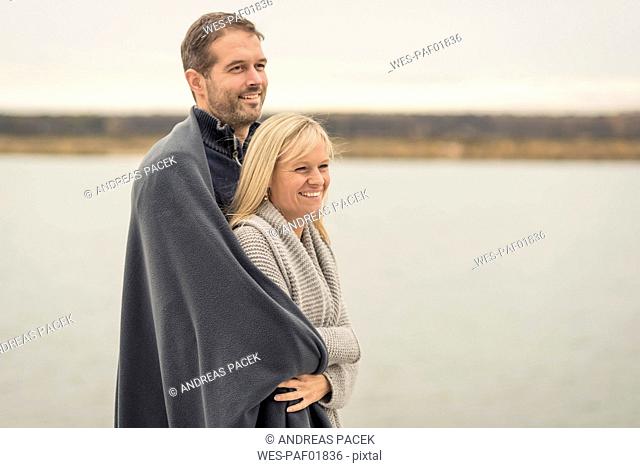 Happy couple standing at lake shore, embracing