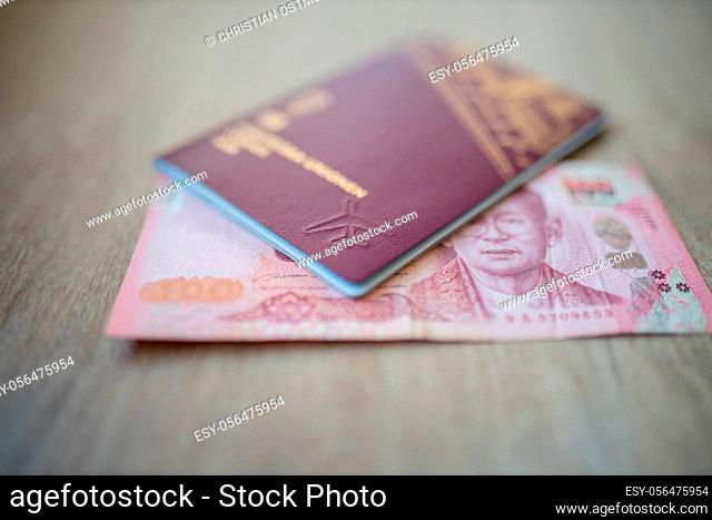 Picture of a 100 Thai Baht Bill Partially Inside a blurry Sweden Passport, showing the face of Bhumibol Adulyadej