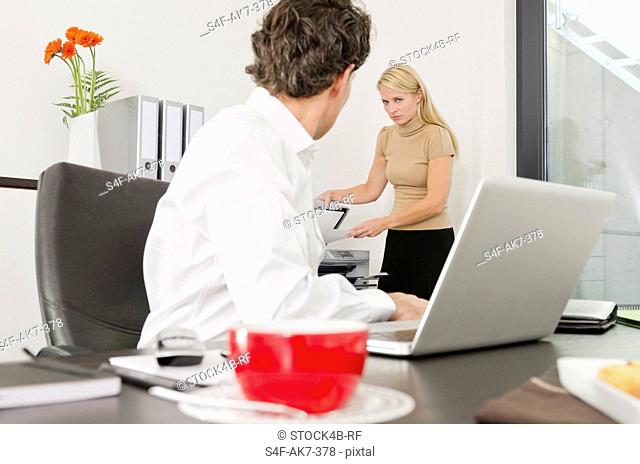 Businessman looking at woman using photocopier