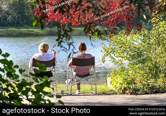24 September 2023, Baden-Württemberg, Ertingen: Two women sitting on camping chairs by a lake in the sun. Photo: Thomas Warnack/dpa