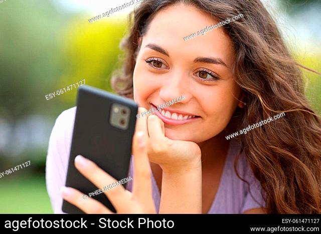 Happy woman reading message on cell phone in a park