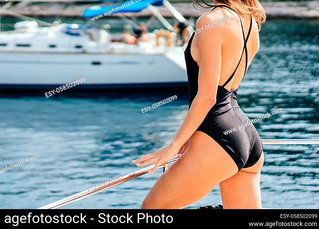 Young slim woman sitting in bikini bathing suit on a yacht in sunglasses near blue sea water