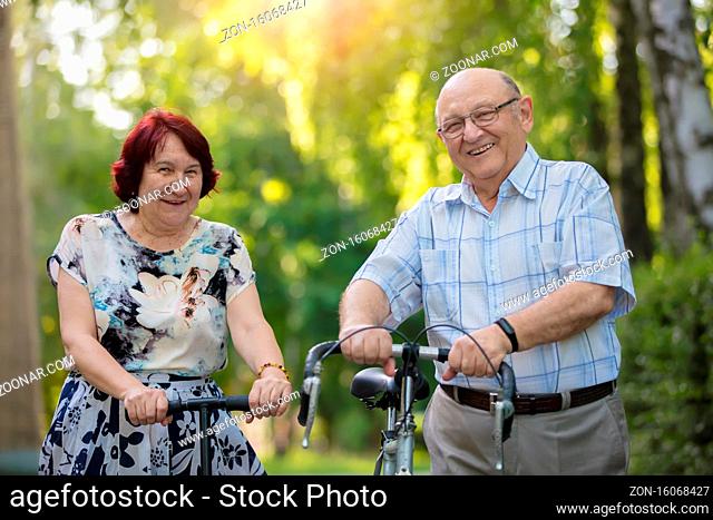 Happy elderly couple with a bicycle. Handsome man and woman senior citizens. Husband and wife of old age for a walk