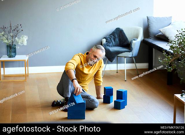 Mature man playing with building blocks on the floor at home