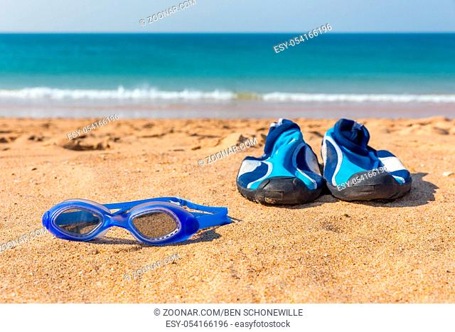 Blue swimming goggles and water shoes lying at coast with sea