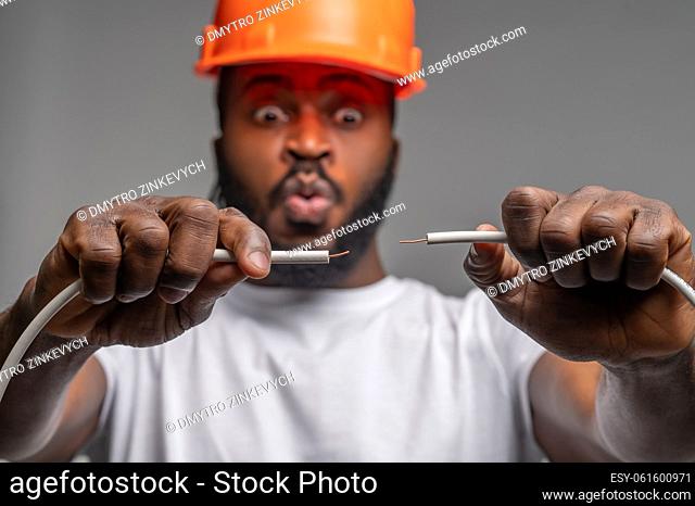 Portrait of a scared electrician in an orange hardhat connecting ends of the stripped electrical wires