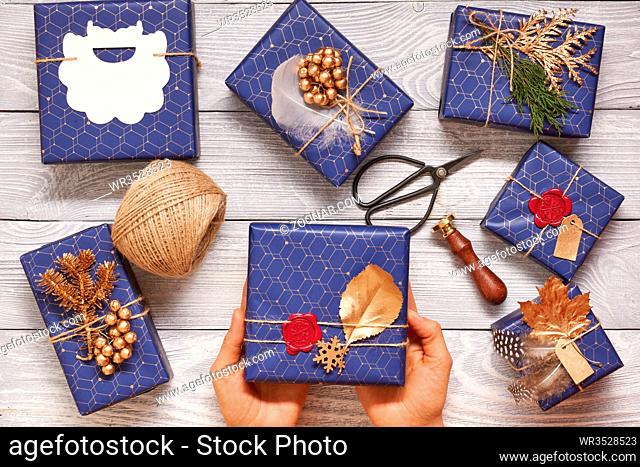 Woman wrapping christmas gifts. Creatively wrapped and decorated christmas presents in boxes on wooden background.Top view from above