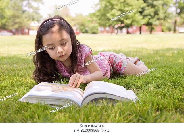 Hispanic girl laying in grass reading book