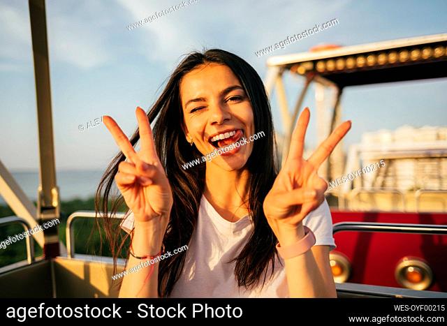 Smiling beautiful woman showing peace sign while enjoying Ferris wheel ride
