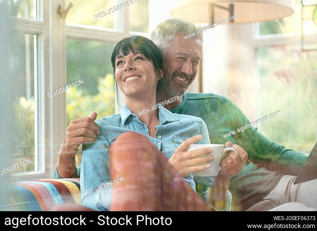 Happy woman with coffee cup by man seen through glass