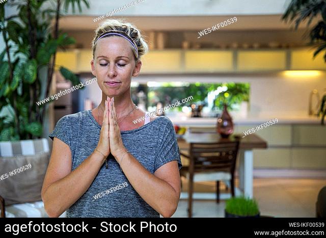 Woman with hands clasped meditating at home