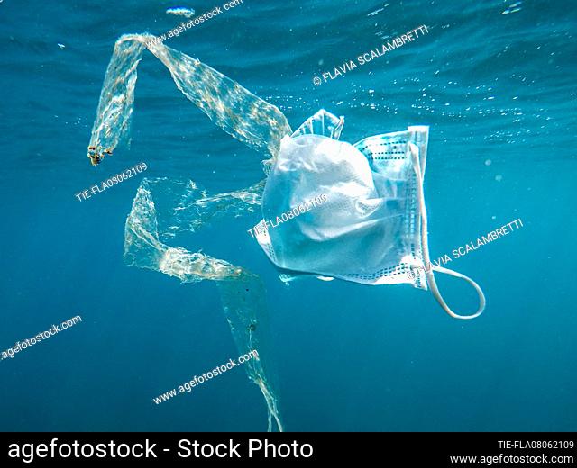 A surgical mask floats in the sea. In the Mediterranean Sea, plastics, microplastics and surgical masks pollute the sea , Ladispoli, ITALY-08-06-2021
