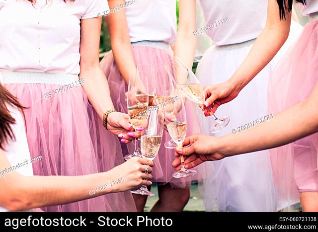 Close view of young girls hands with glasses of champagne. Cropped photo of bride and her girlfriends, all in pink fluffy skirts