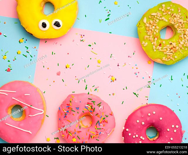 whole round pink donuts with colored sprinkles lie on a blue-pink background, top view, pastel colors