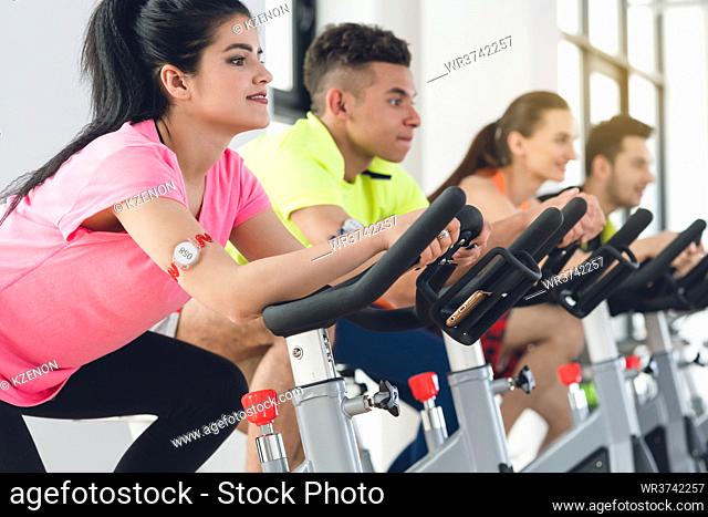 Smiling young healthy woman cycling at gym