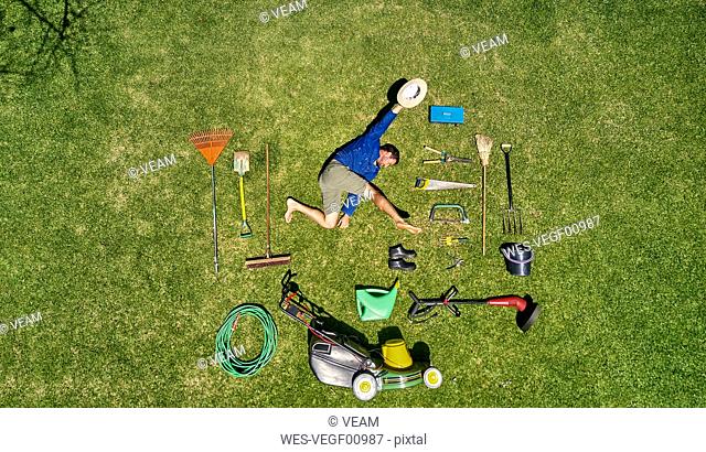 View from above of a gardener in laying on the grass with all the tools he need for take care of garden