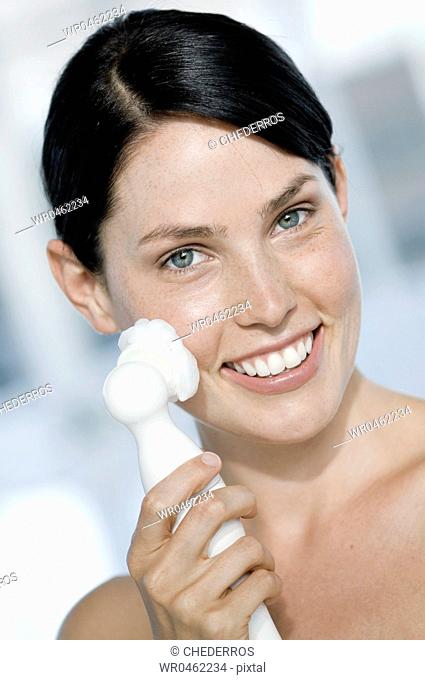 Portrait of a young woman using a massager on her face