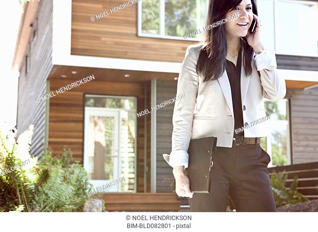 Mixed race real estate agent standing near house talking on cell phone