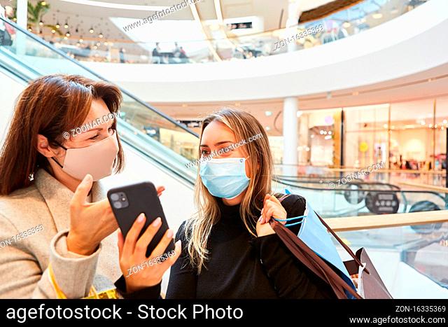 Zwei Freundinnen mit Smartphone und Mundschutz wegen Covid-19 beim Shopping