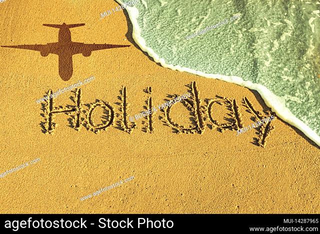 The word holiday written in the sand by the sea, shadow of a plane