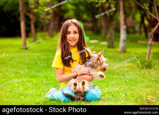 The cute little girl with a funny yorkshire terrier dog sitting on the lawn in the backyard