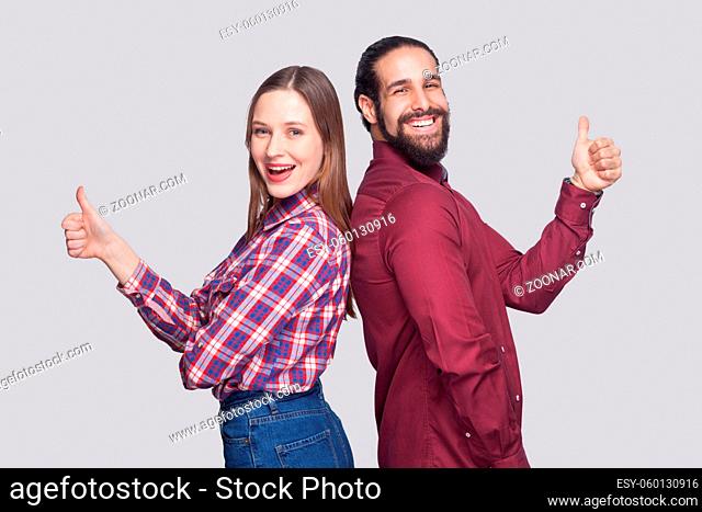 Profile side view portrait of happy satisfied bearded man and woman in casual style standing and looking at camera, smiling with thumbs up