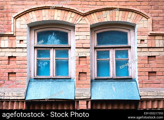 Two vintage arched windows in a wall of yellow bricks. Green - the colors of sea wave glass in a maroon dark red wooden frame