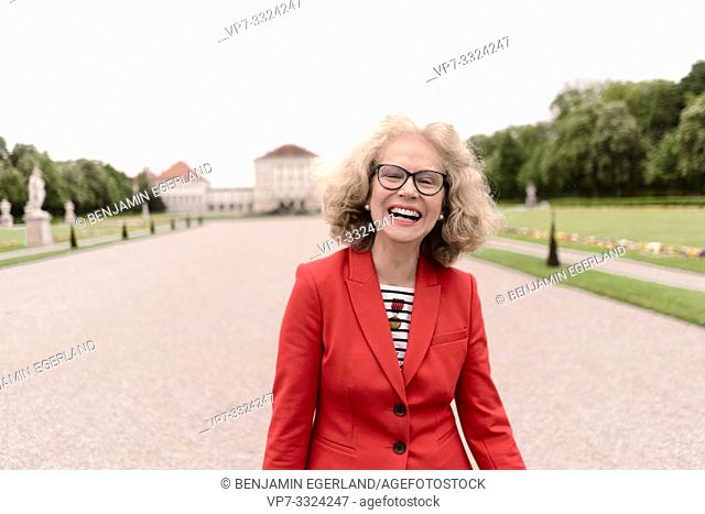 happy senior woman (67 years old) laughing in park at touristic sight Nymphenburg palace, in Munich, Germany