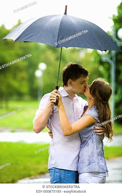 Portrait of romantic couple embracing and kissing each other under umbrella during rain