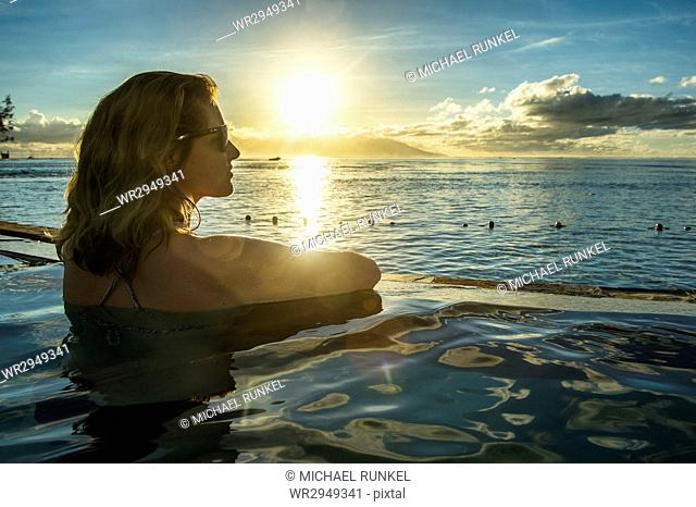 Woman enjoying the sunset in a swimming pool with Moorea in the background, Papeete, Tahiti, Society Islands, French Polynesia, Pacific