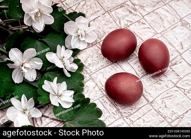 On the table next to the blooming daffodils are three red Easter eggs. Top view, close-up