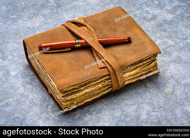 antique leatherbound journal with decked edge handmade paper pages and a stylish pen on a handmade bark paper, journaling concept