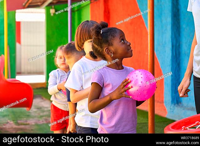 Multikulturelle Gruppe Kinder beim Ball spielen draußen vor der Kita